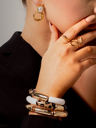 Woman wearing gold and pearl jewellery from the Élégance Collection, including bold bracelets, earrings, and rings.