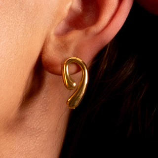 Close-up of the Amanda Twist Earrings in polished gold, featuring a curved loop design worn on the ear.