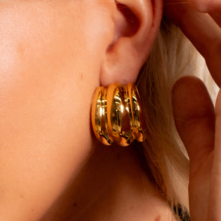 Close-up of triple stacked gold hoop earrings on ear, polished bold finish from the Nashville Collection.