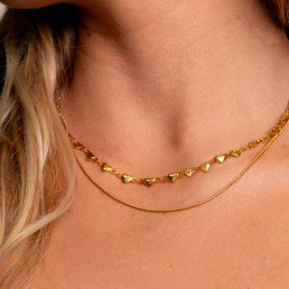 Detailed close-up of the gold heart-link necklace paired with a simple gold chain on the neck.