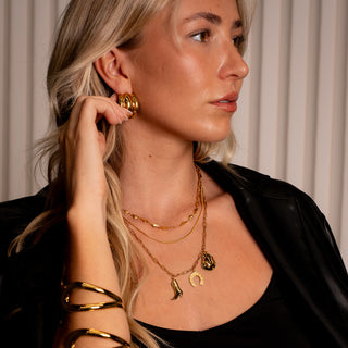 Model wearing the Nashville Charm Necklace layered with gold chains, styled with gold hoops and a black outfit.