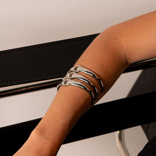 Close-up of a person's arm wearing multiple silver bracelets against a neutral background