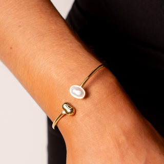 Athena Pearl Bangle 18k gold asymmetric imitation pearl and gold orb open cuff bangle close up on wrist
