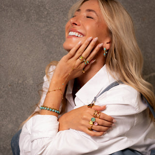 Model smiling and wearing the Aurora Prism Ring with colourful stones, paired with layered gold jewellery and turquoise accents.