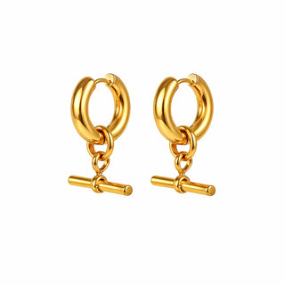 Close-up of gold huggie hoop earrings with a dangling T-bar charm, featuring thick rounded hoops and a high-shine 18k gold finish. Photographed on a clean white background to highlight the polished, modern design.